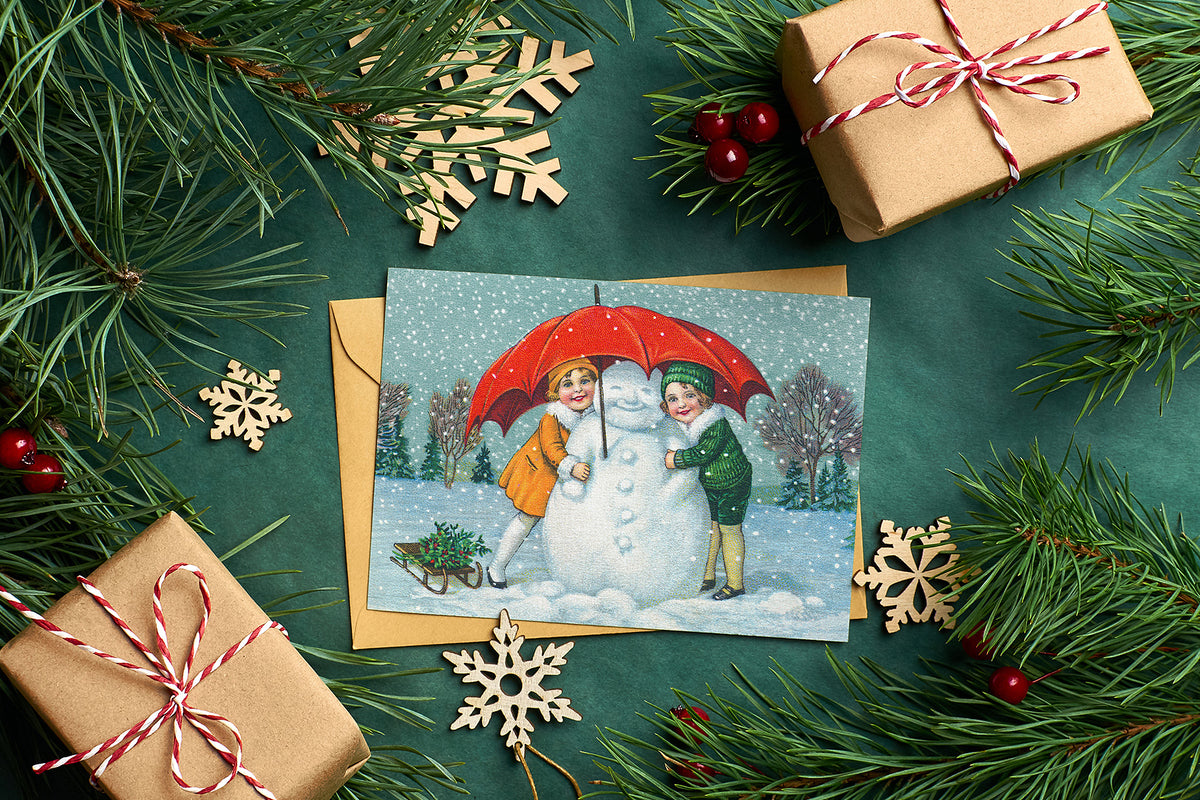 Vintage Christmas illustration of a boy and girl building a snowman, shown as a holiday card design example.
